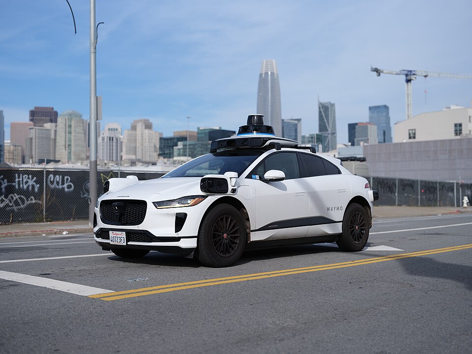 A Waymo Jaguar I-Pace with its roof sensors on a San Francisco street, 2023. The photographer reports it was driving itself with no one in the driver's seat.